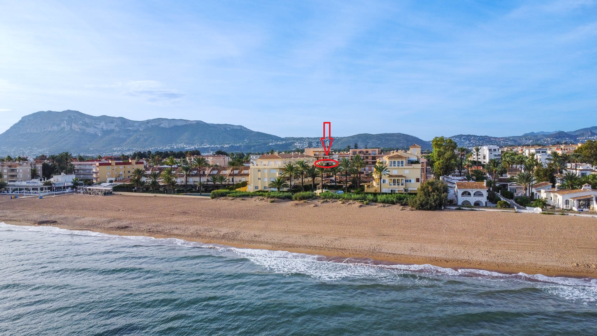 Vue aérienne d'un complexe d'appartements en bord de mer avec l'unité indiquée, offrant un accès direct à la plage et une vue sur les montagnes.