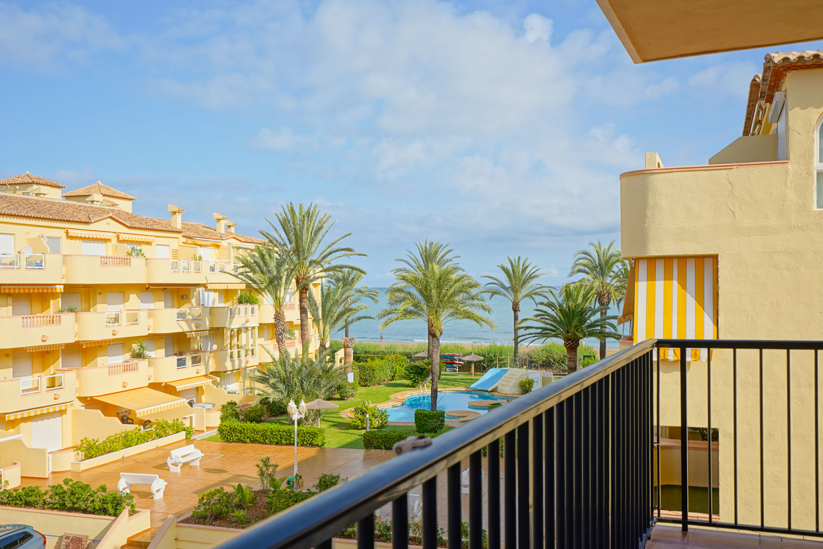 Vue depuis un balcon privé sur un complexe résidentiel avec piscine, jardins paysagers et vue imprenable sur la mer Méditerranée.