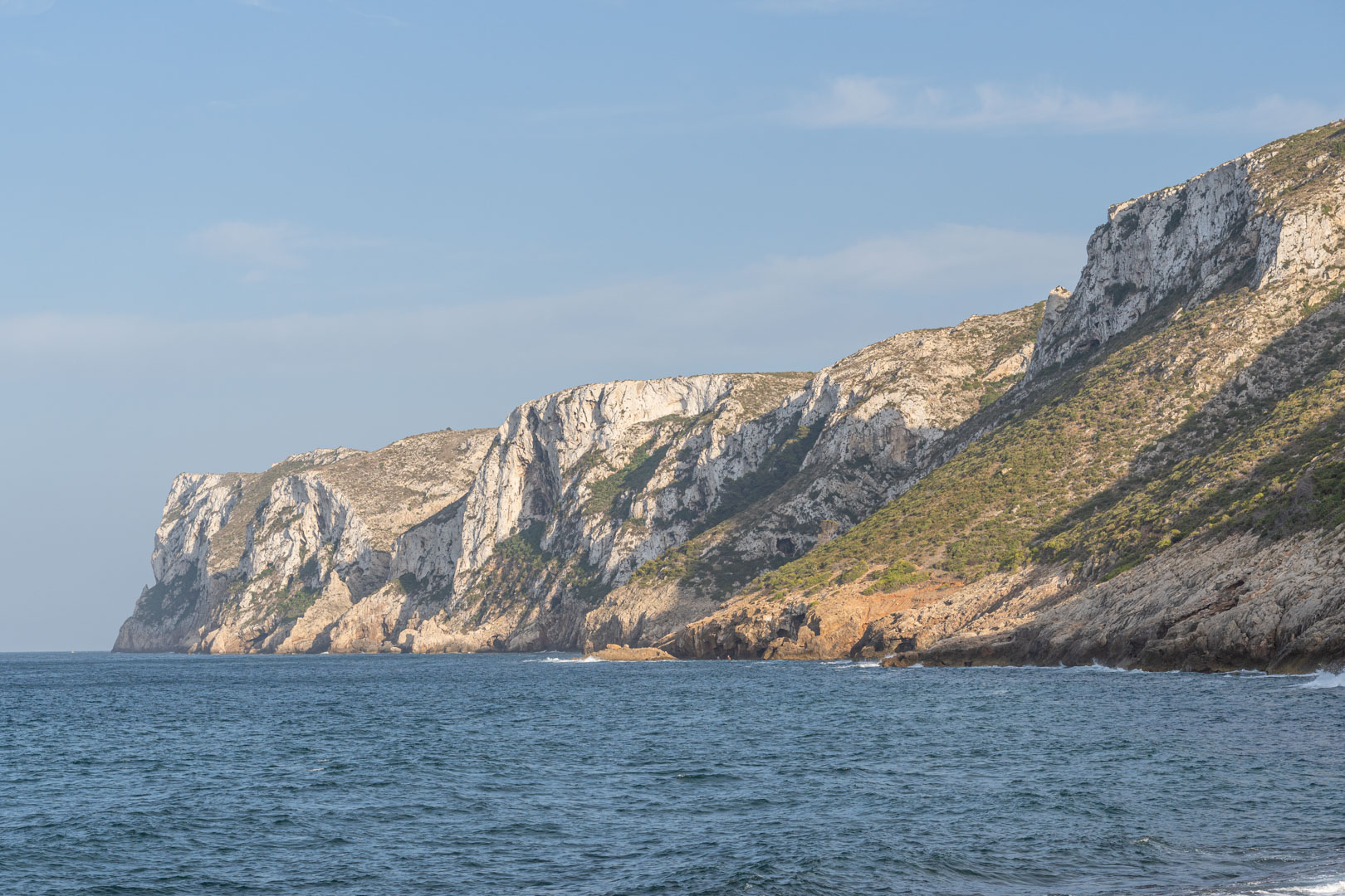 Vue panoramique de falaises calcaires escarpées surplombant la mer Méditerranée, avec une végétation côtière éparse et des formations rocheuses naturelles.