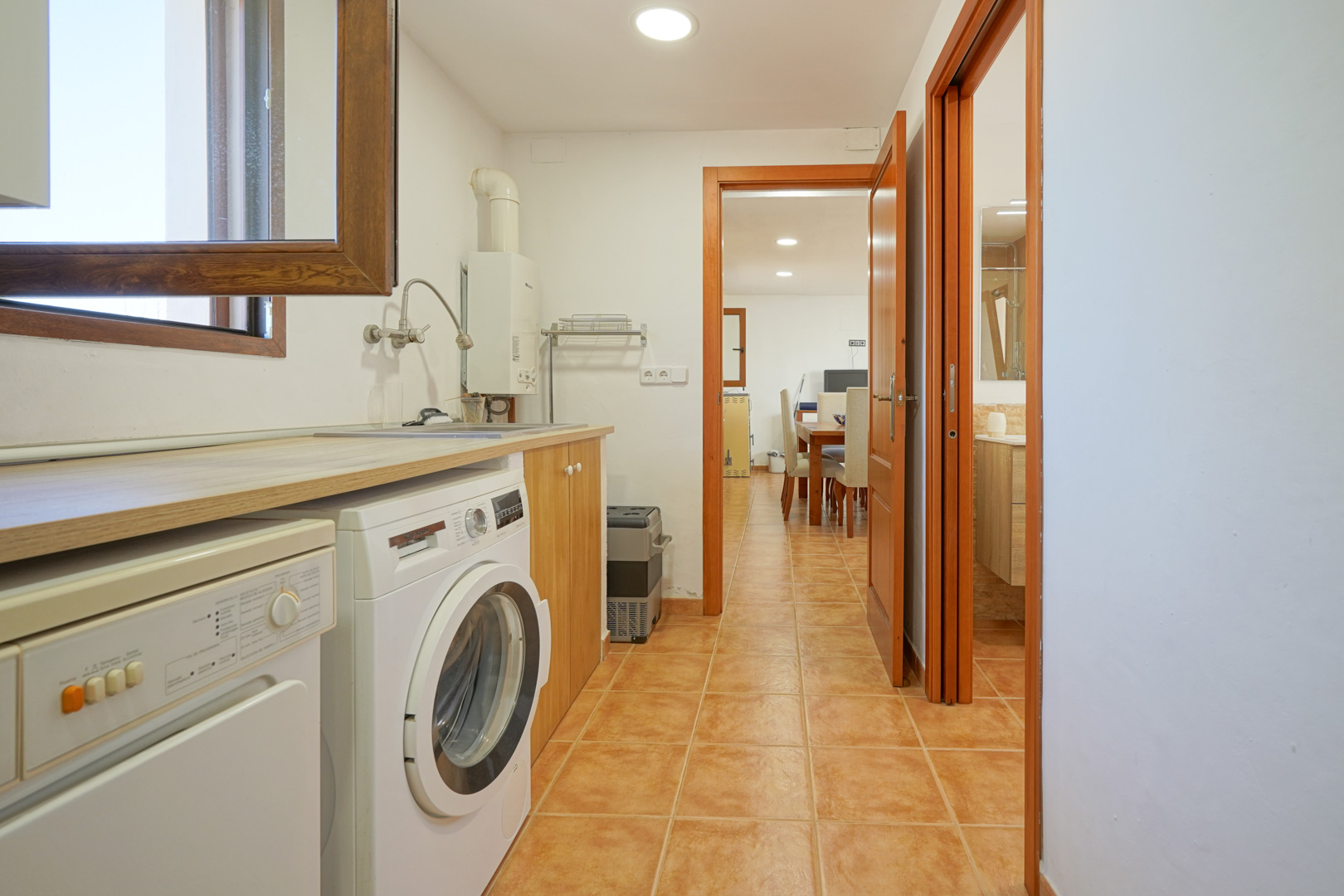 Buanderie pratique avec plan de travail en bois, lave-linge et évier, offrant une transition fluide vers la salle à manger et une salle de bain.