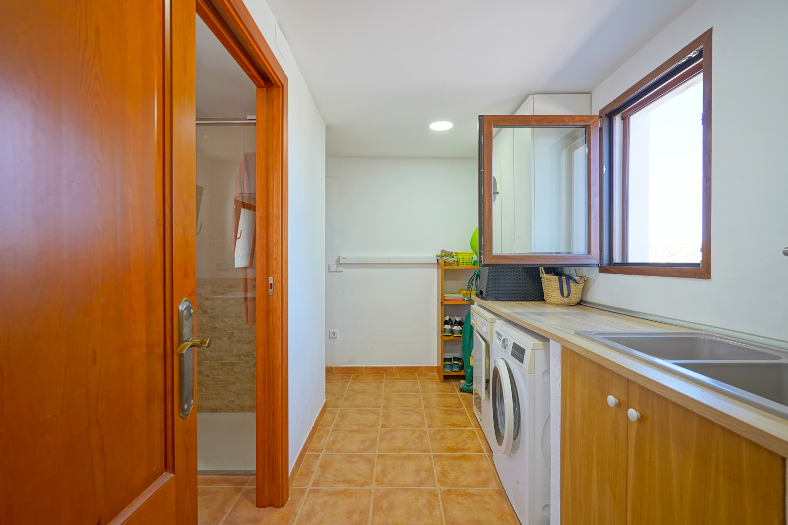 Buanderie spacieuse équipée d'un lave-linge, d'un sèche-linge et d'un double évier, offrant un accès direct à une salle de douche.
