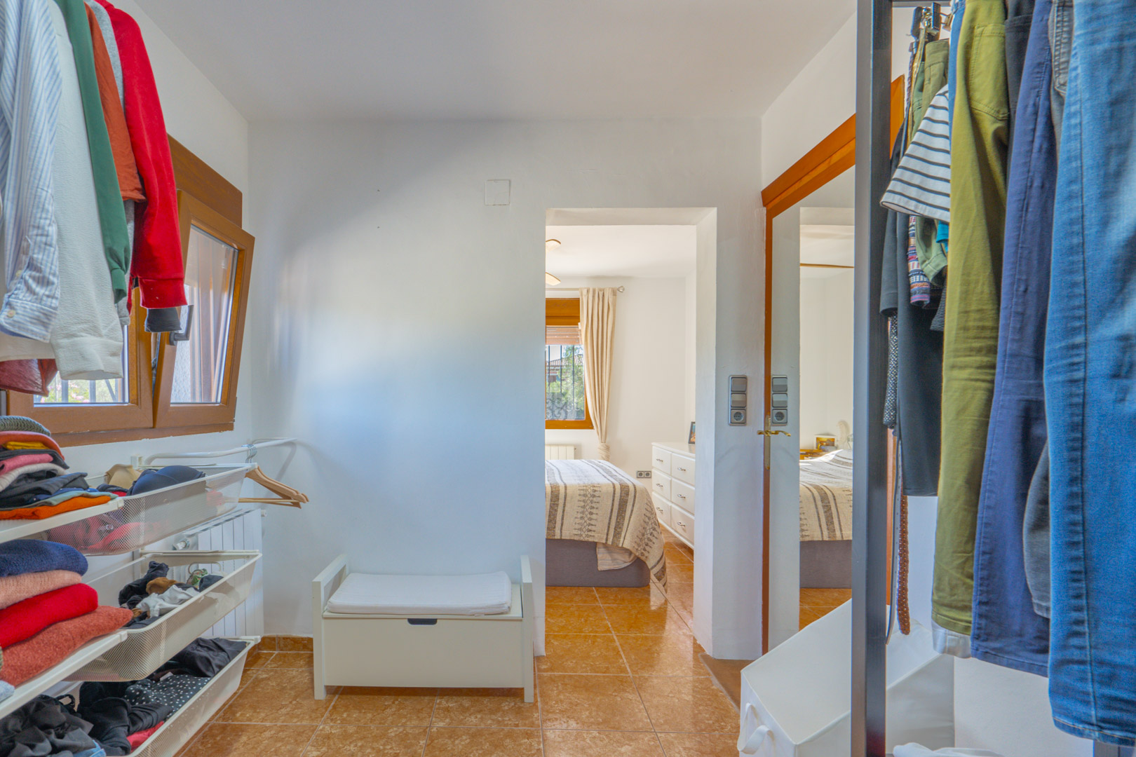 Dressing fonctionnel avec étagères ouvertes, tiroirs en filet et penderies, offrant un accès direct à la chambre avec un sol en grès cérame.