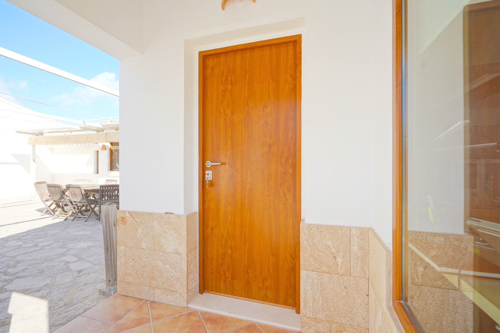 Entrée principale avec porte en bois, soubassement en pierre naturelle et accès à une terrasse pavée équipée d'un coin repas extérieur.