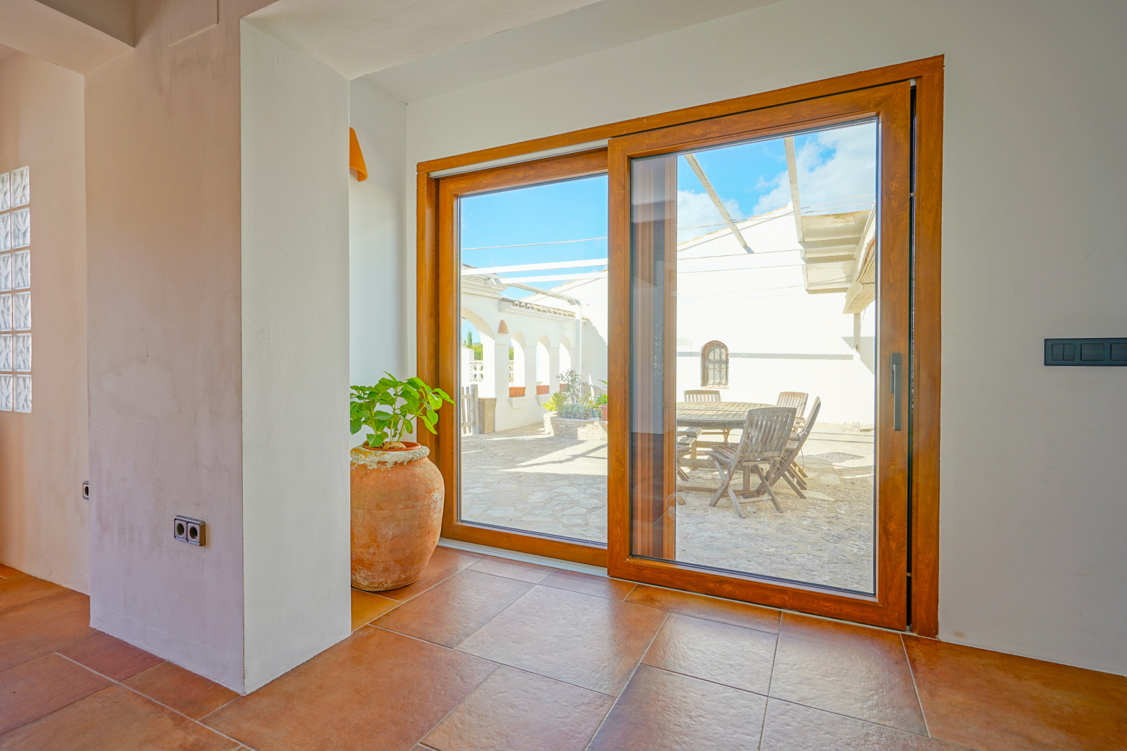 Grande baie vitrée coulissante avec cadre en bois reliant l'intérieur en terre cuite à un patio en pierre doté d'un coin repas extérieur.