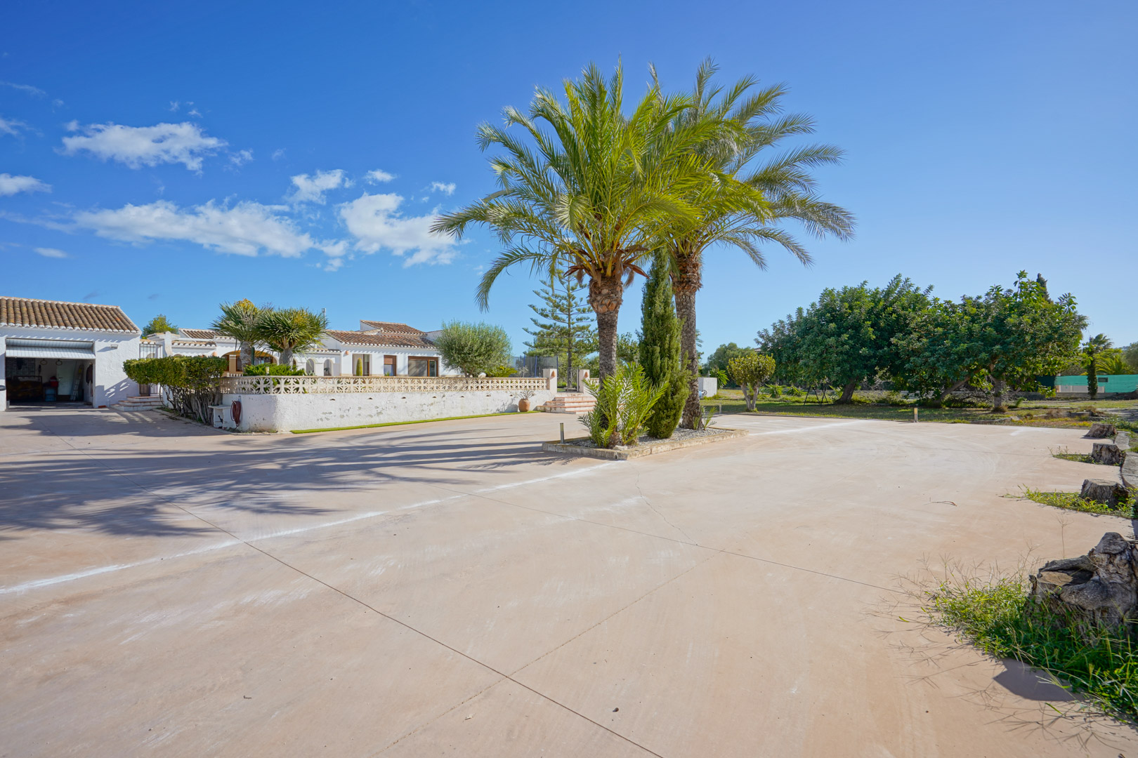 Large allée pavée avec des palmiers centraux, offrant un accès direct au garage et à la villa blanche de style méditerranéen.