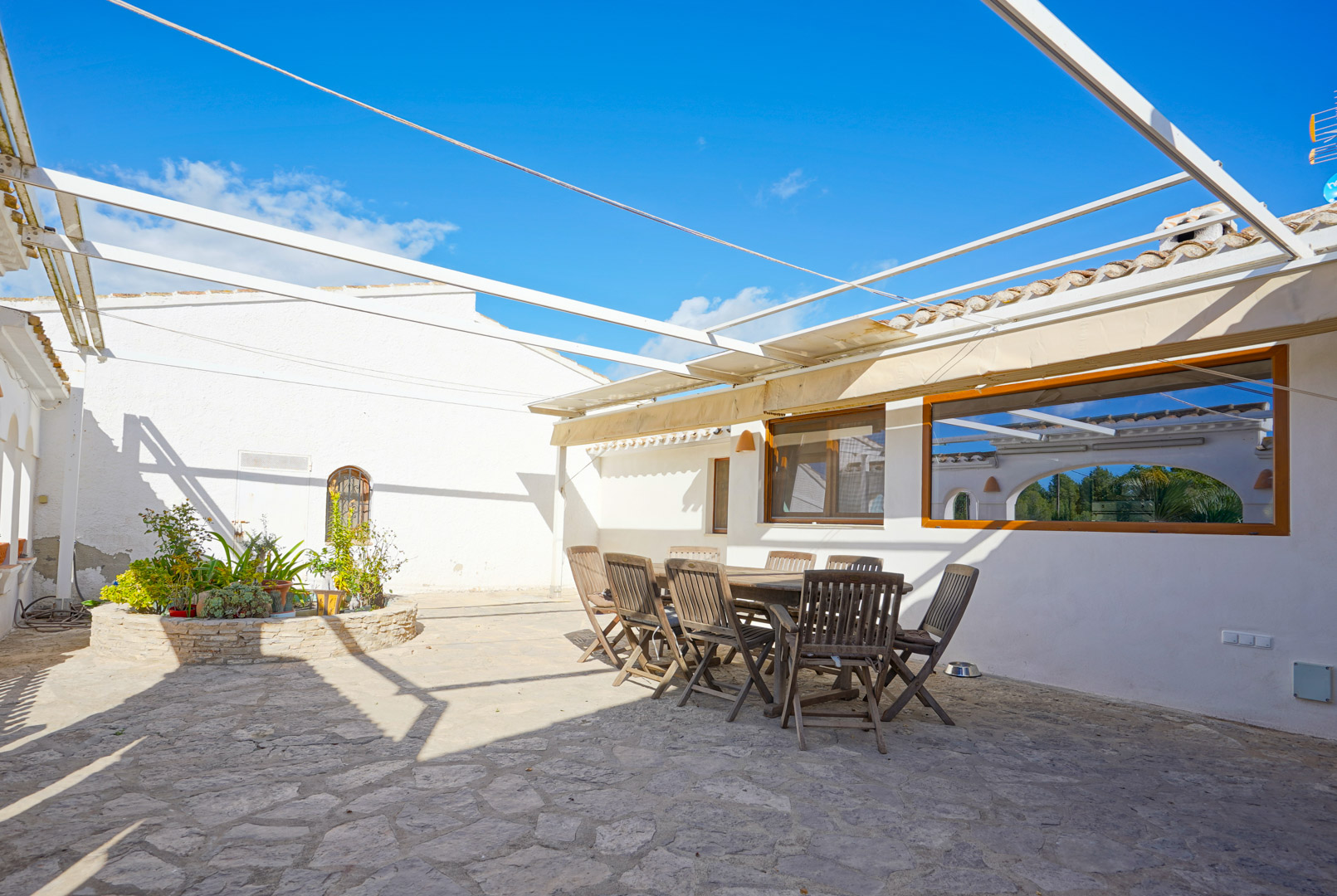 Terrasse extérieure avec sol en pierre naturelle, ensemble de repas en bois et structure de pergola métallique sous un ciel dégagé.