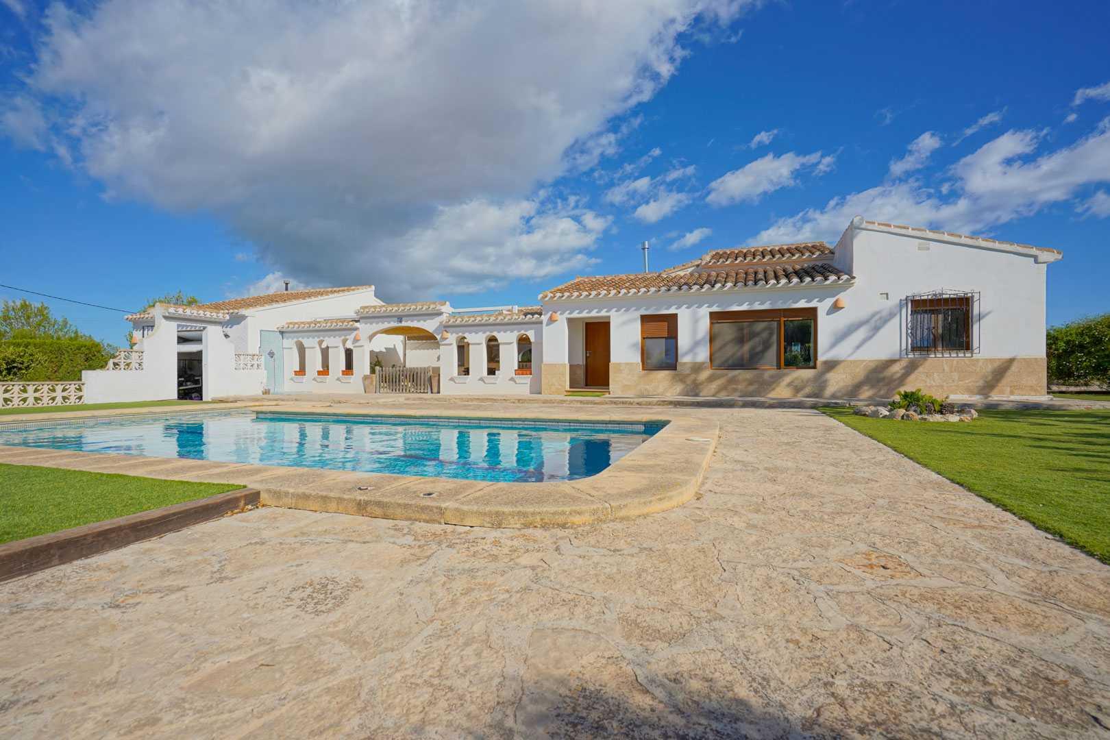 Vue extérieure de la villa avec piscine privée, terrasse en pierre naturelle et espaces verts soignés, reflétant l'architecture méditerranéenne.