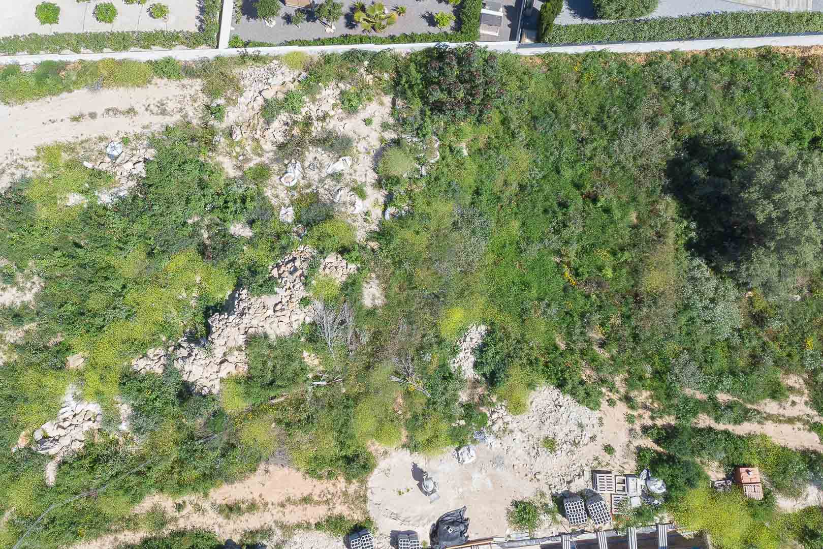 Vue aérienne zénithale du terrain de 1 000 m², illustrant le relief naturel, la végétation locale et les premiers matériaux de construction.