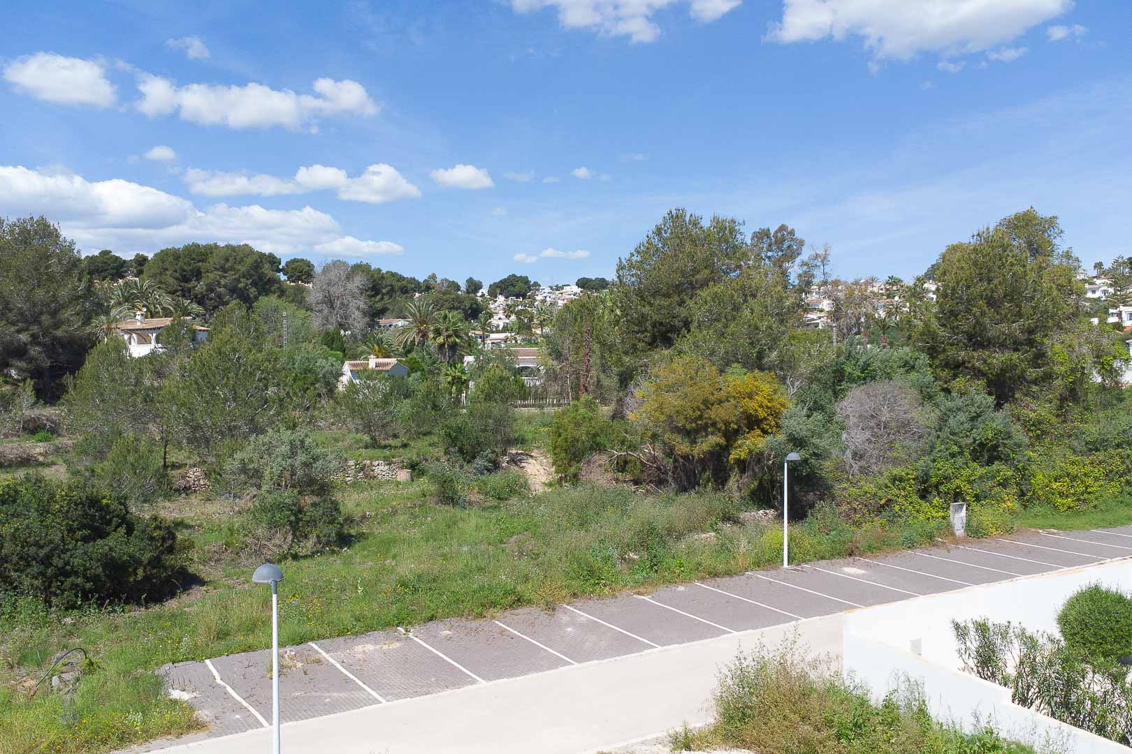 Vues panoramiques depuis la propriété sur le paysage méditerranéen, avec une végétation dense, des habitations voisines et une zone de stationnement extérieure.