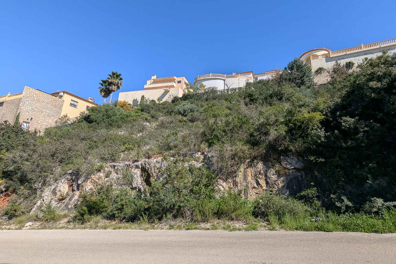 Vue extérieure d'une villa en construction à Pedreguer, Costa Blanca, entourée de végétation méditerranéenne et de roches naturelles.