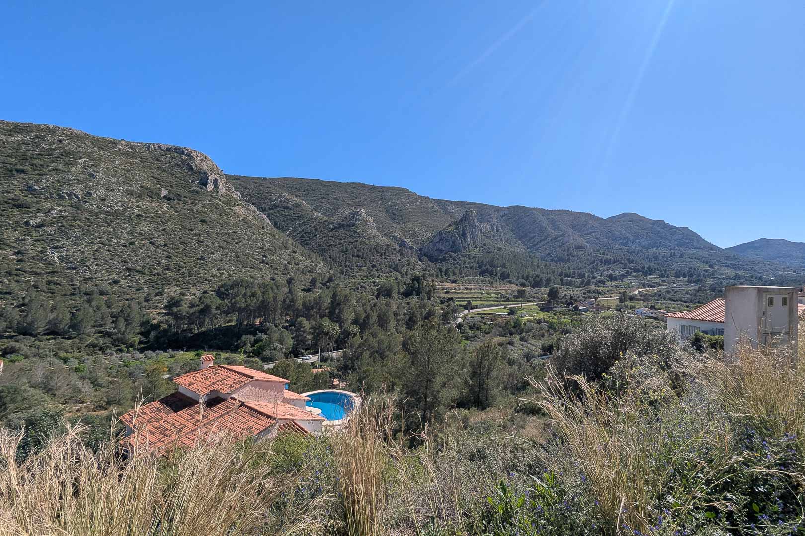 Vues panoramiques sur la vallée et les montagnes de Pedreguer, mettant en valeur la végétation locale et une villa avec piscine en contrebas.