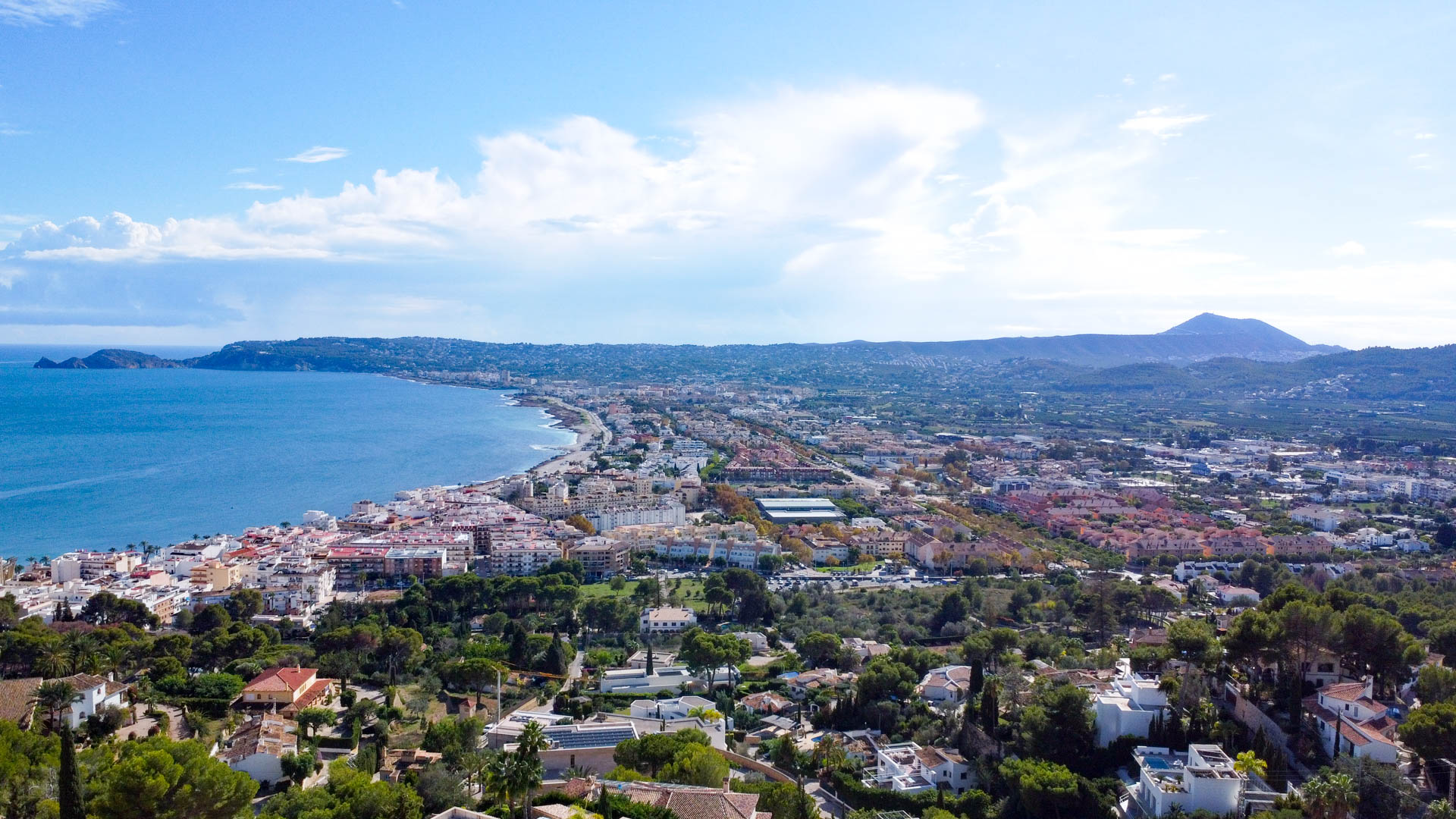 Vue aérienne panoramique sur la baie de Jávea et le port depuis La Corona, avec la côte méditerranéenne et le mont Montgó à l'horizon.