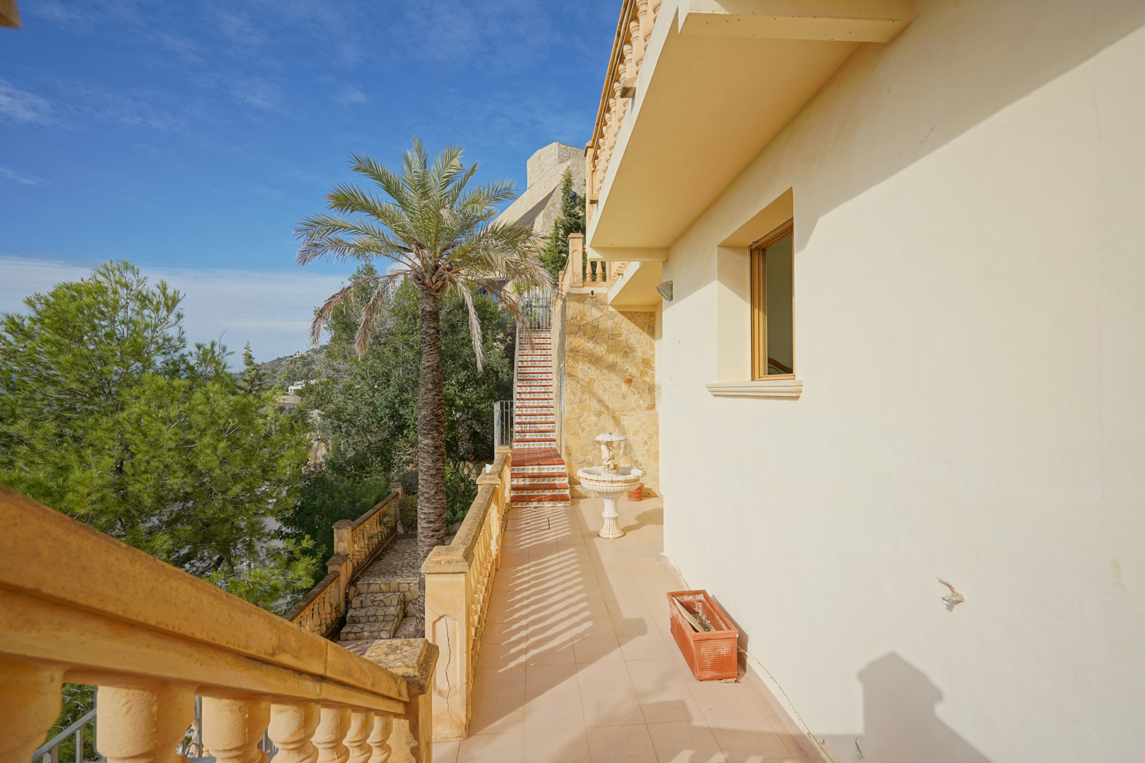 Allée extérieure avec balustrades classiques, murs en pierre naturelle et escalier orné de carreaux traditionnels bordant une végétation méditerranéenne.