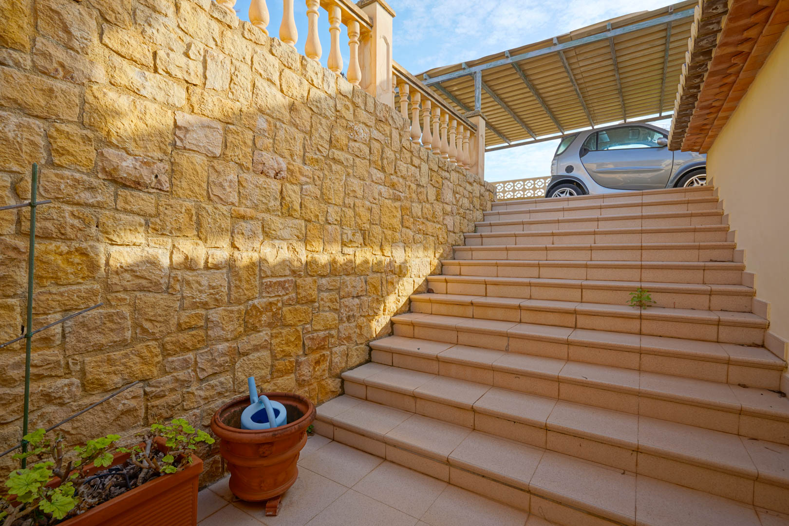 Escalier extérieur en grès bordé d'un mur en pierre naturelle, reliant les niveaux de la villa à l'espace de stationnement couvert.