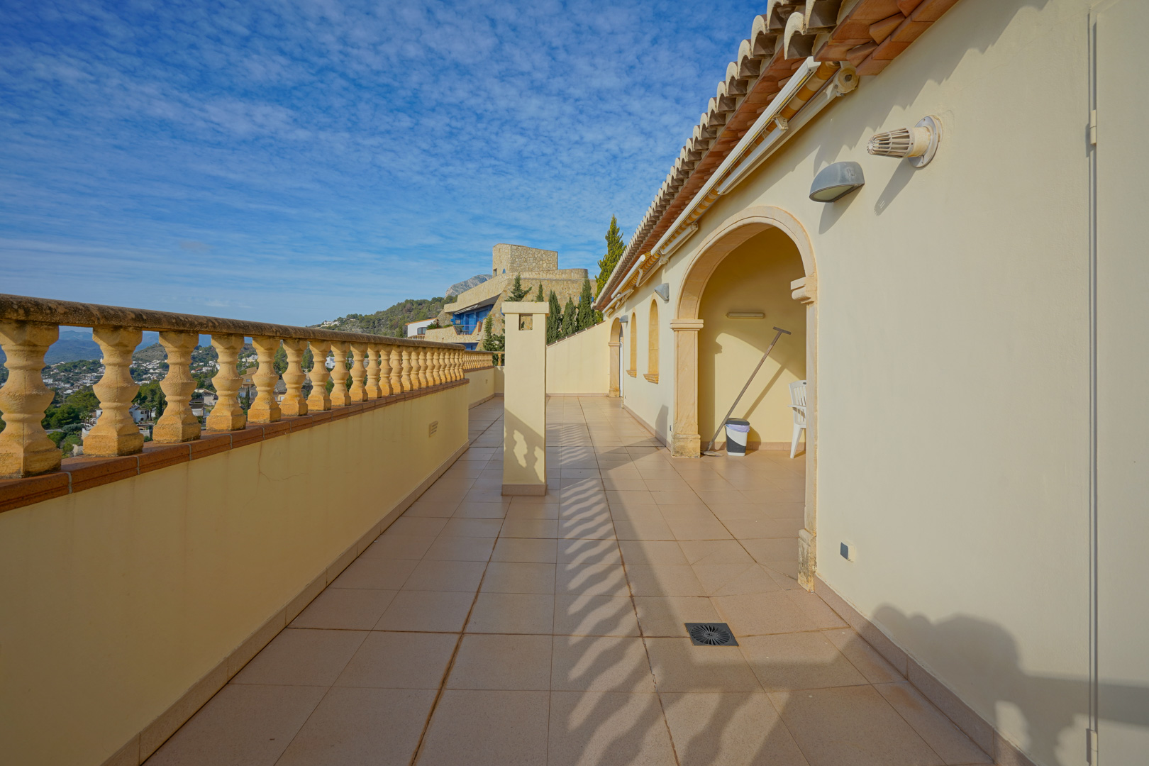 Longue terrasse avec balustrade traditionnelle en pierre et sol en grès, offrant une vue dégagée sur la vallée sous une toiture en tuiles méditerranéennes.