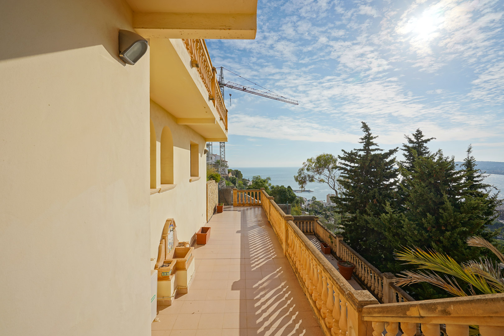 Longue terrasse avec balustrade traditionnelle, fontaine murale décorative et vue panoramique sur la baie de Jávea et la mer Méditerranée.