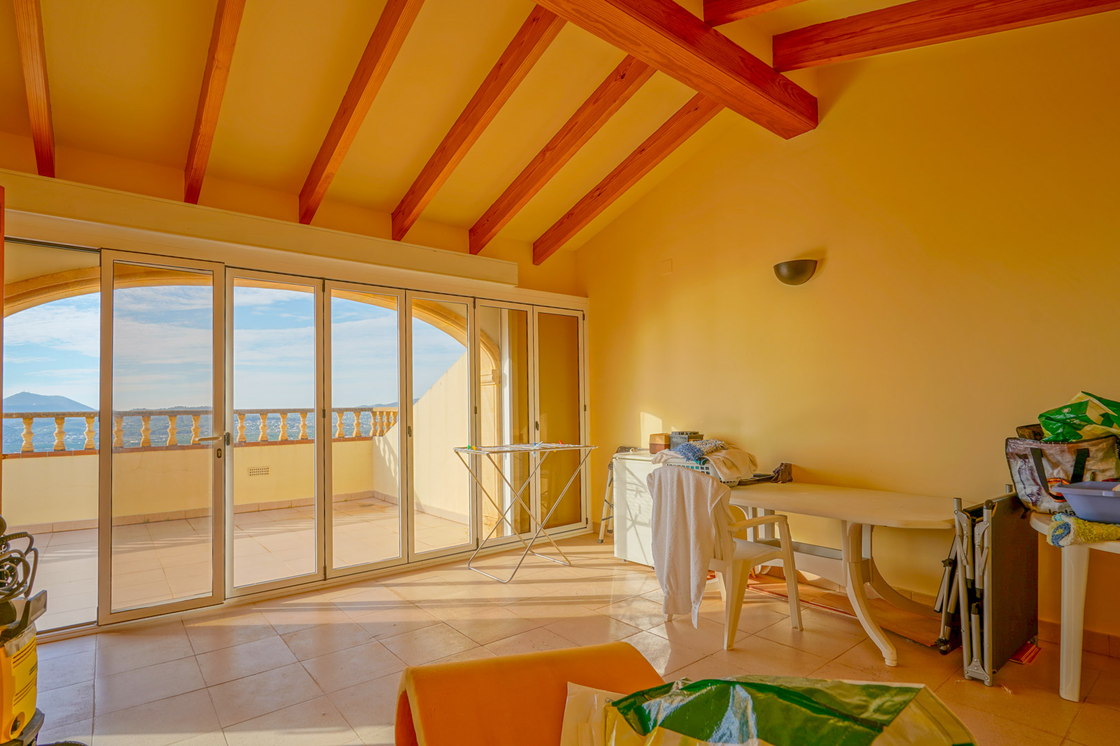 Pièce à l'étage supérieur dotée de hauts plafonds aux poutres apparentes et de grandes baies vitrées menant à une terrasse avec vue sur les montagnes.