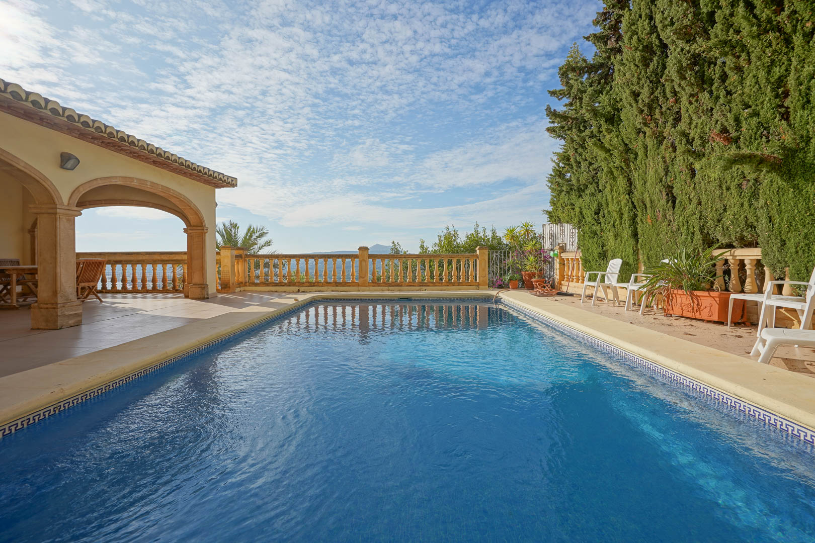 Piscine rectangulaire bordée de pierre, jouxtant une terrasse couverte aux arches traditionnelles et une balustrade classique offrant une vue dégagée.