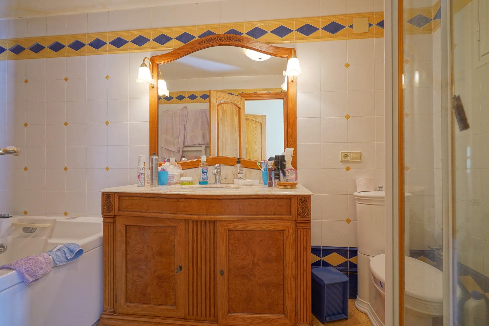Salle de bains traditionnelle avec meuble en bois sculpté, plan de travail en marbre et carrelage mural orné de motifs bleus et jaunes.