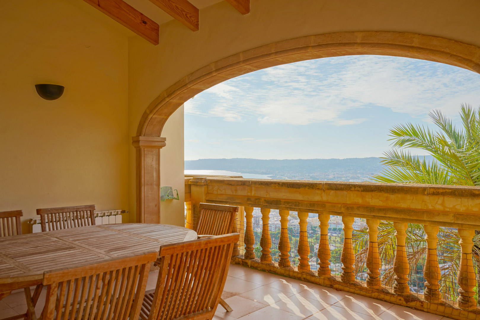 Terrasse couverte avec arche en pierre, plafond à poutres en bois et coin repas offrant une vue panoramique sur la baie de Jávea et les montagnes.