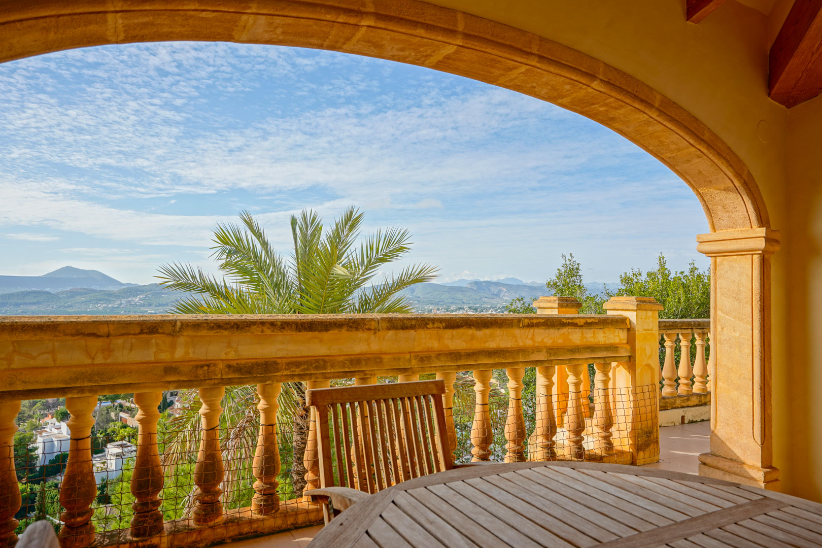 Terrasse couverte avec arche en pierre traditionnelle et balustrade, offrant une vue panoramique sur les montagnes et la vallée avec du mobilier en bois.