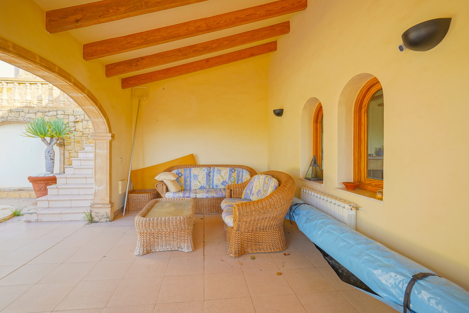 Terrasse couverte avec poutres en bois apparentes, mobilier en osier et arches traditionnelles offrant un espace de détente ombragé près de la piscine.