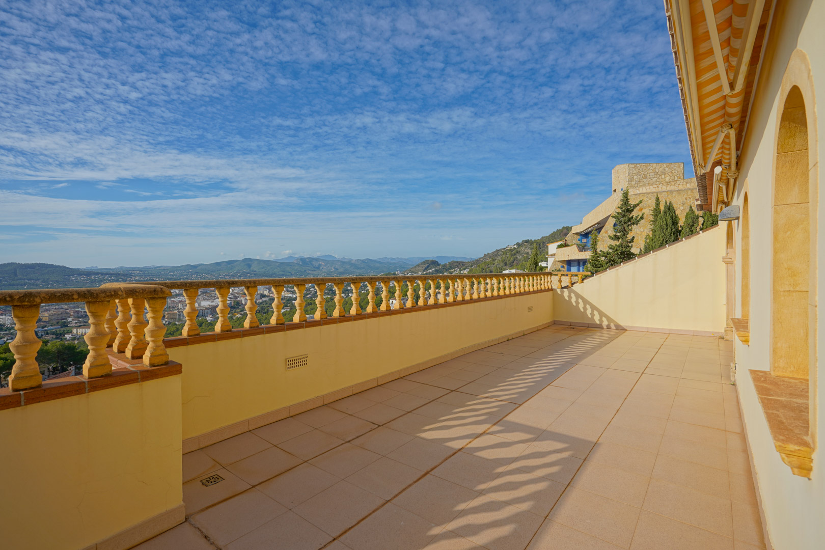Terrasse supérieure avec balustrade traditionnelle et sol en grès, offrant une vue panoramique sur la vallée de Jávea et les reliefs montagneux environnants.