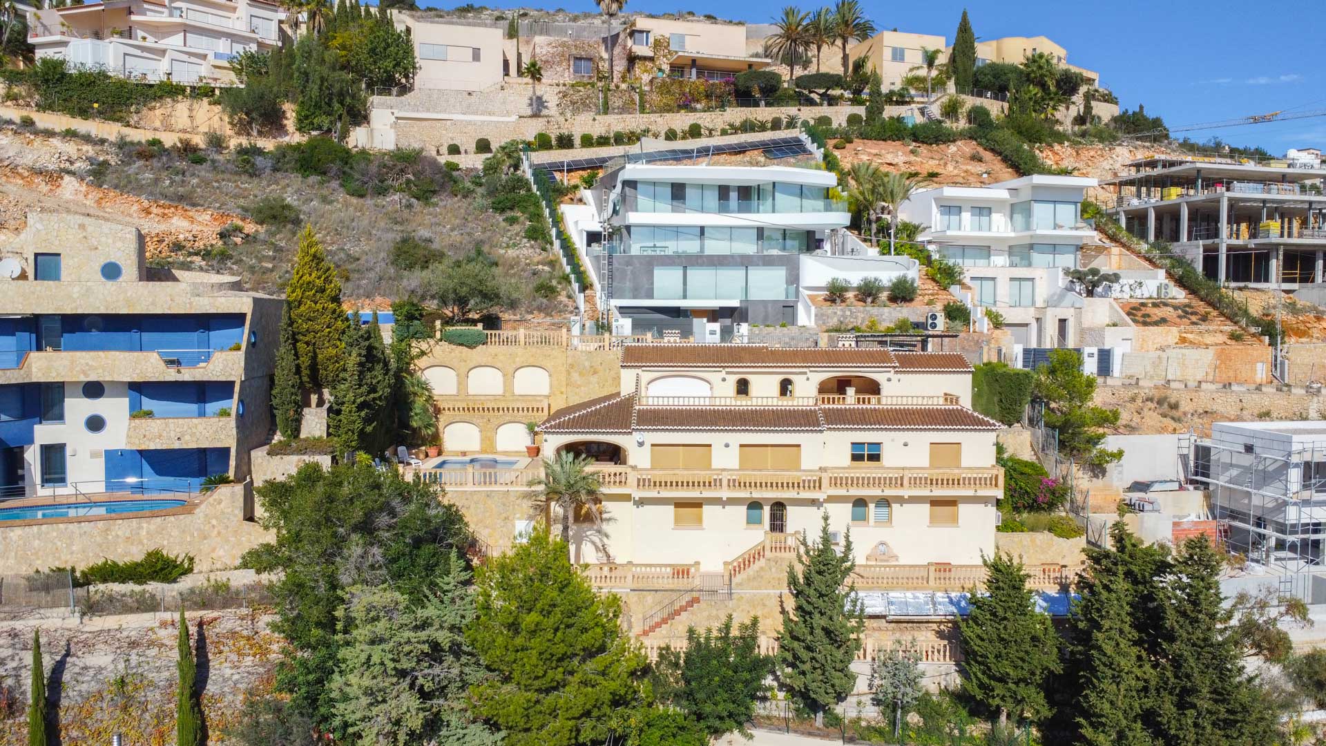 Vue extérieure de la villa traditionnelle à La Corona, présentant une façade crème, des toits en tuiles et des terrasses à balustrades intégrées dans la pente de la colline.