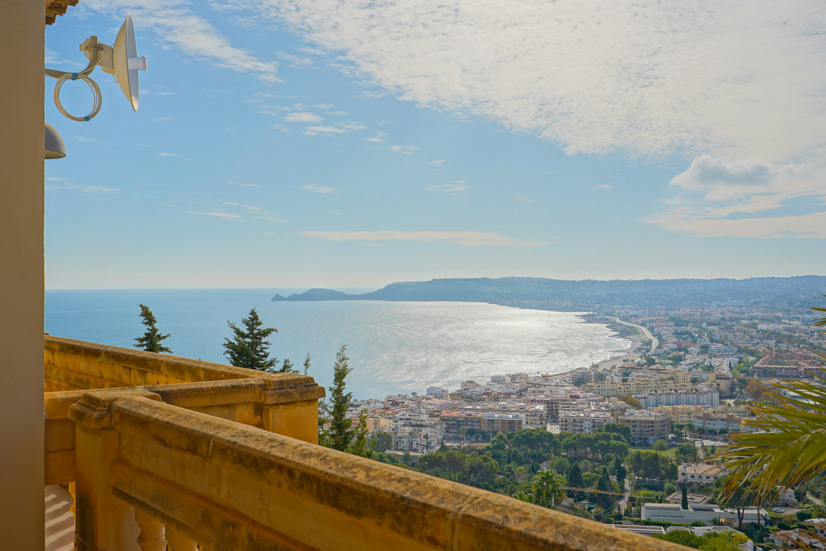 Vue panoramique depuis la terrasse supérieure sur la baie de Jávea et le Cap Negre, avec une balustrade en pierre traditionnelle et un paysage côtier.