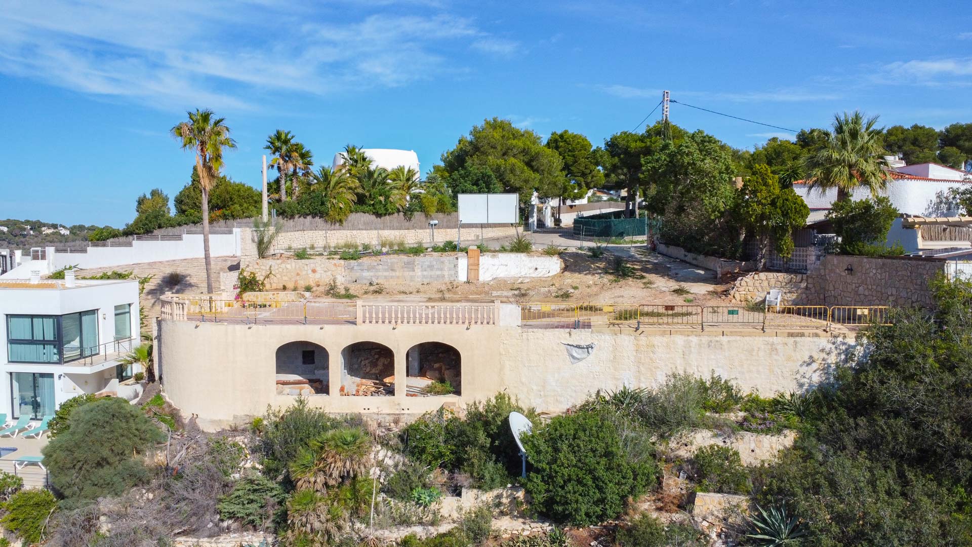 Terrain constructible surélevé avec structure voûtée existante, murs de soutènement en pierre et végétation méditerranéenne, prêt pour une villa de luxe.