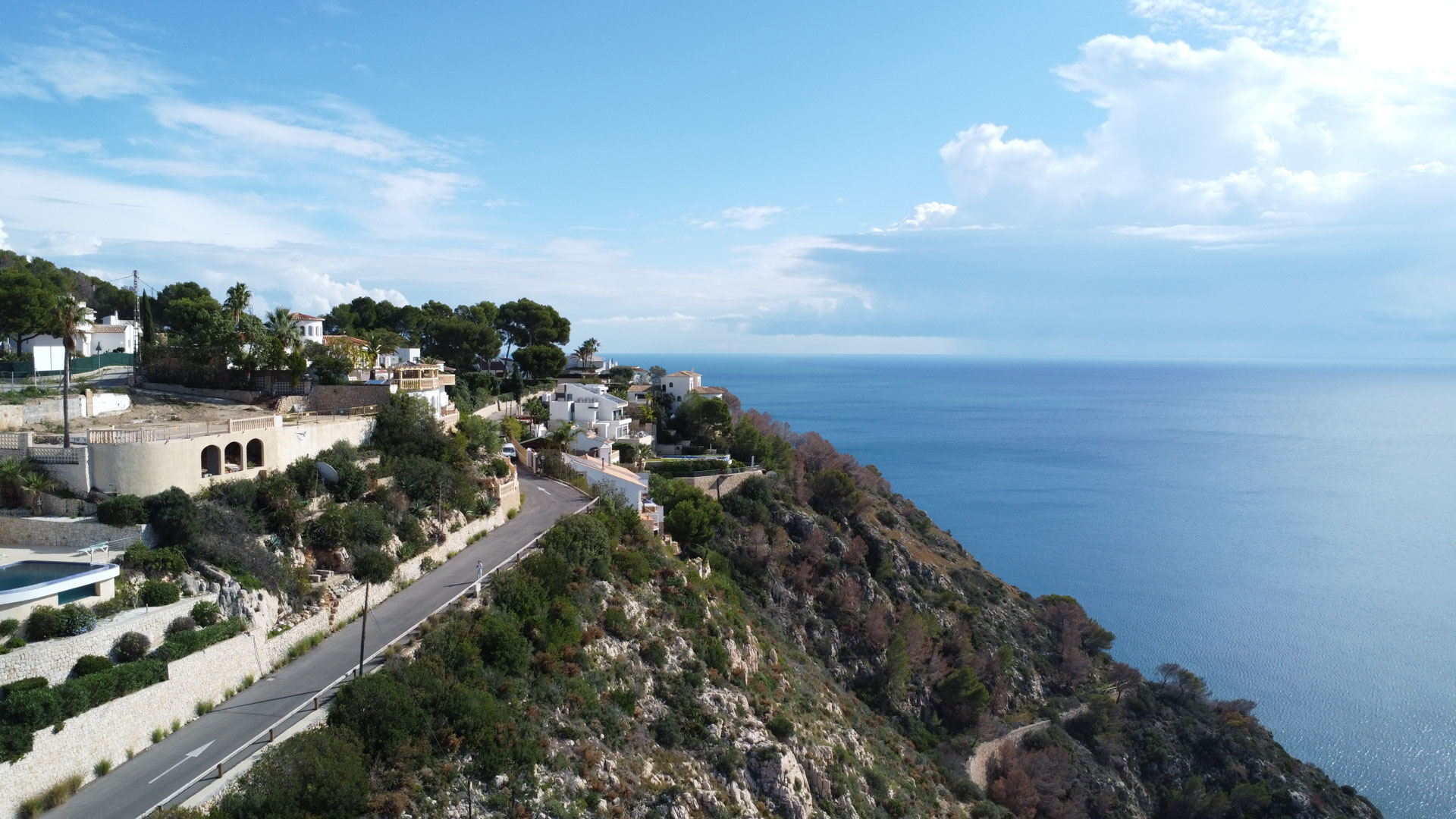 Vue aérienne de la côte de Granadella à Jávea, présentant des terrains en pente avec vue sur la mer Méditerranée et accès par route goudronnée.