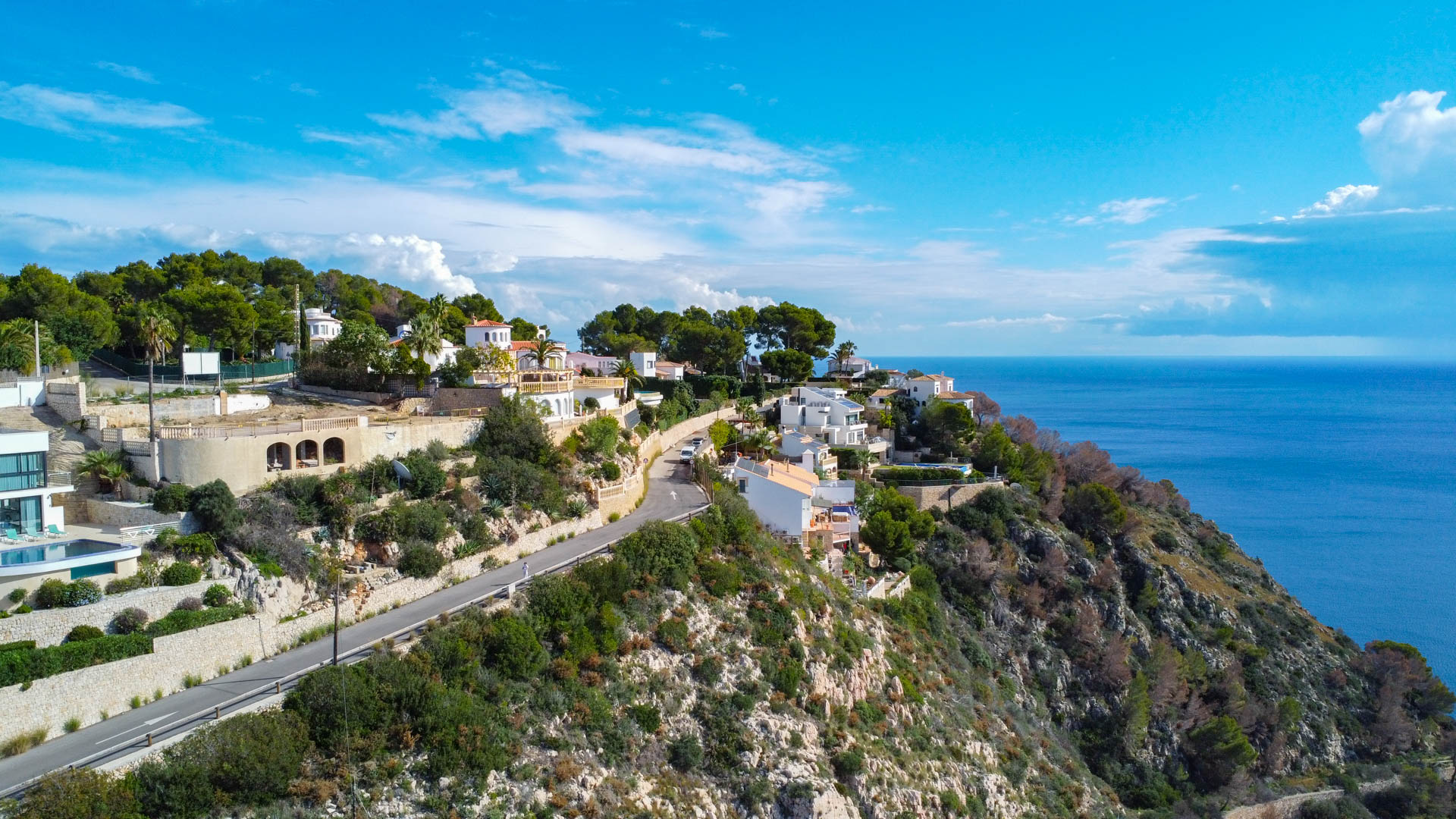 Vue aérienne du terrain en pente à Granadella, illustrant l'accès routier et le panorama dégagé sur la mer Méditerranée et les falaises environnantes.