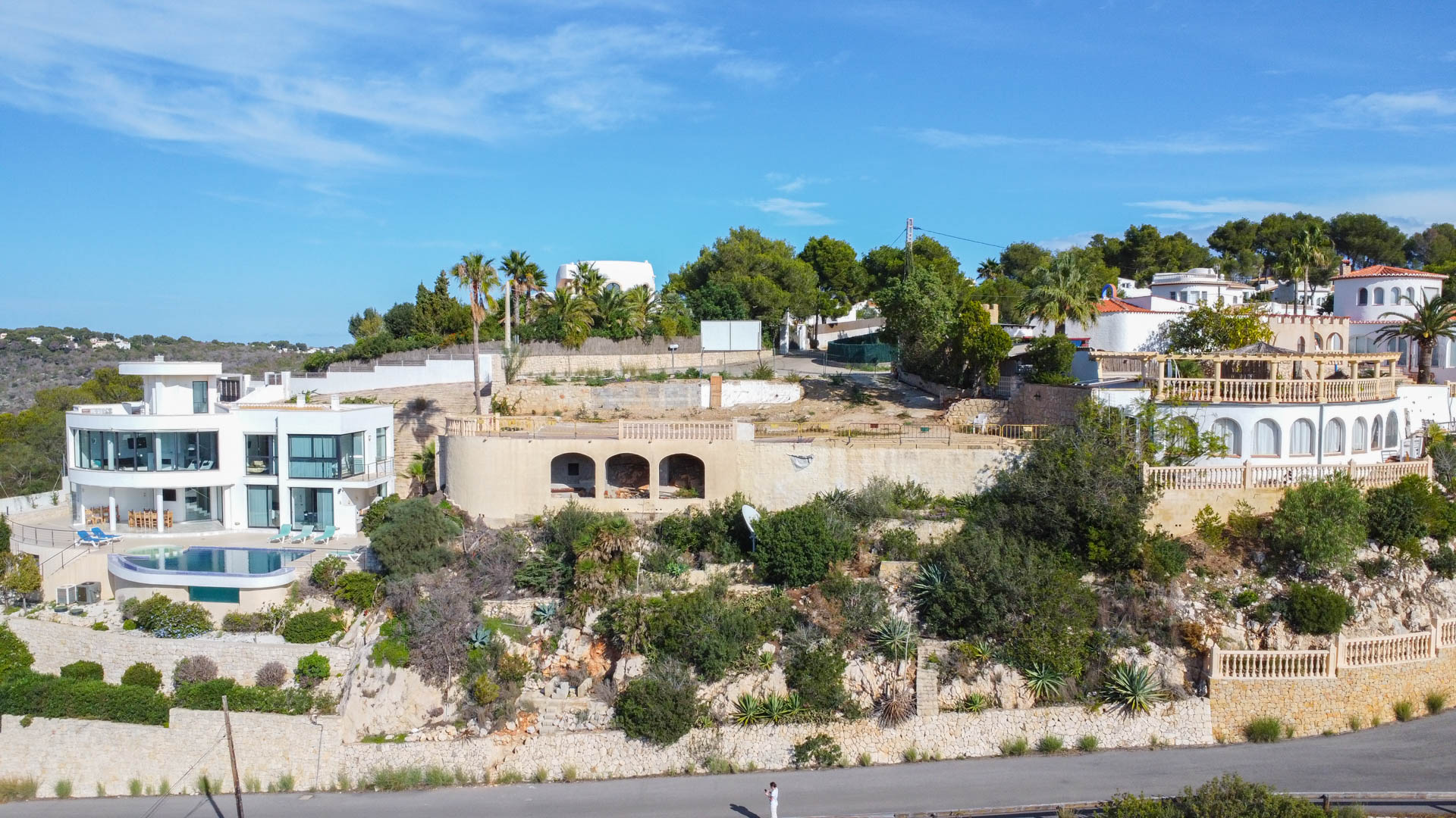 Vue aérienne du terrain surélevé avec fondations en pierre voûtées, entouré de villas de luxe et d'une végétation méditerranéenne sur des murs de soutènement.