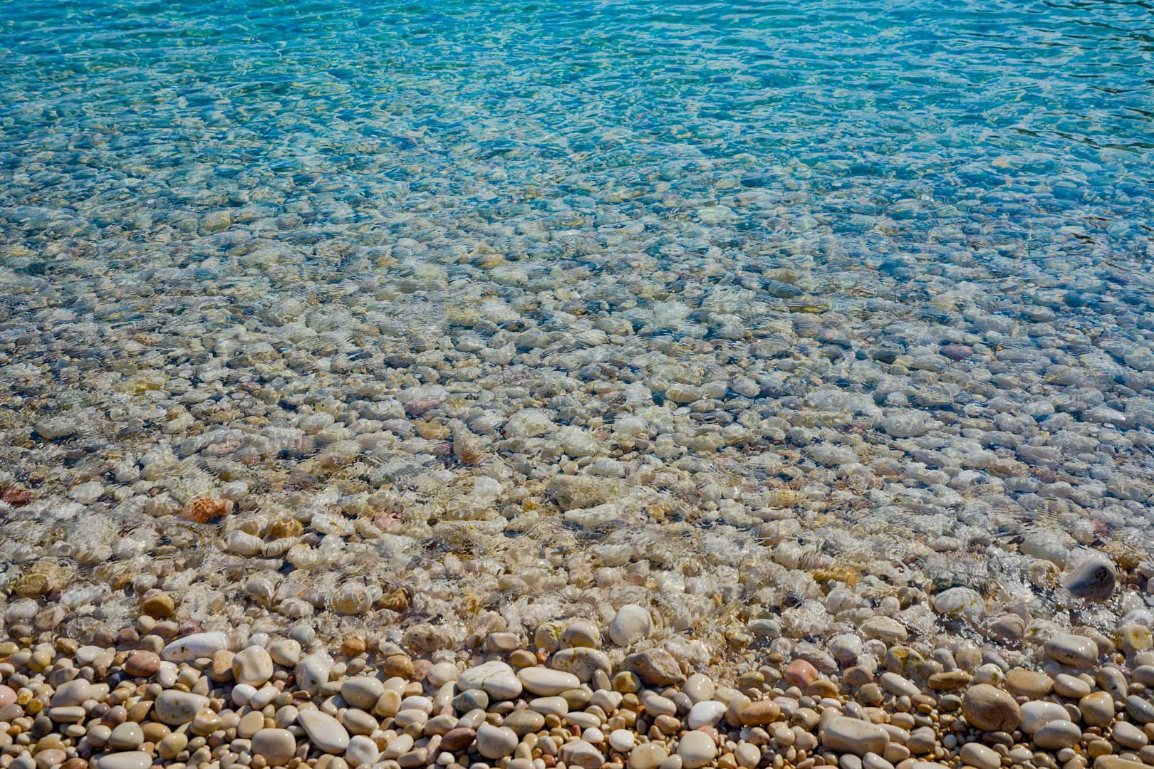 Vue détaillée du rivage de la plage de Granadella, montrant les galets blancs polis et les eaux turquoises cristallines de la Méditerranée.