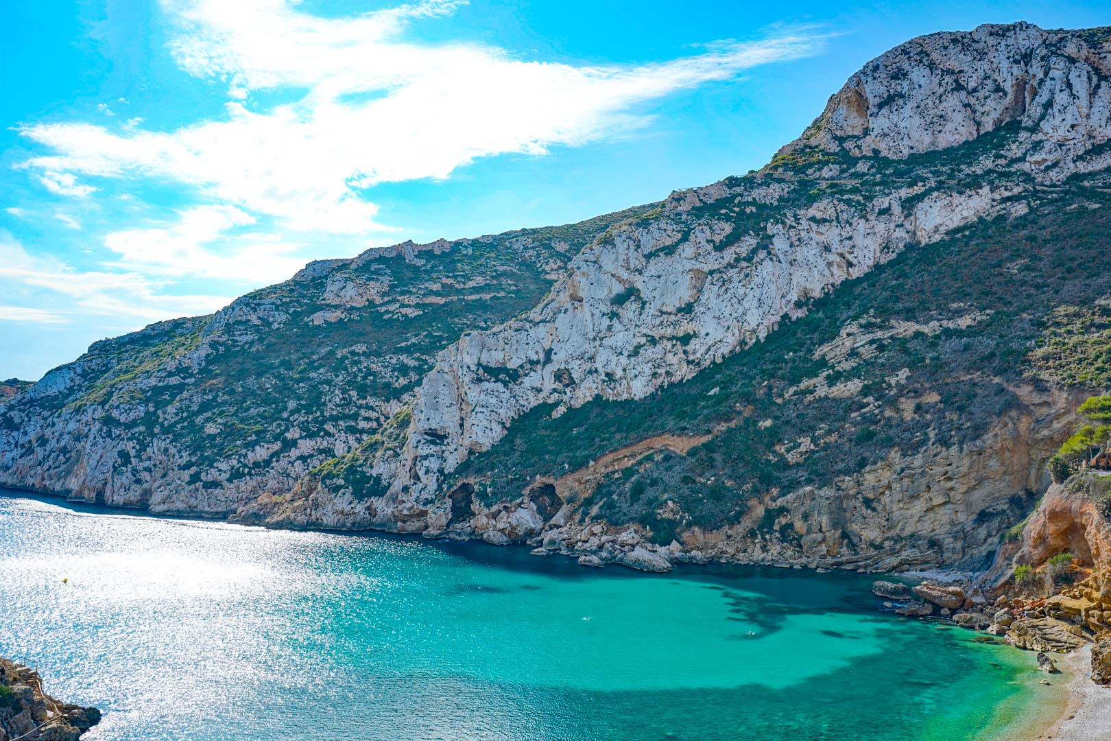 Vue panoramique sur les eaux turquoise de la Cala Granadella, entourée de falaises calcaires escarpées et de végétation méditerranéenne.