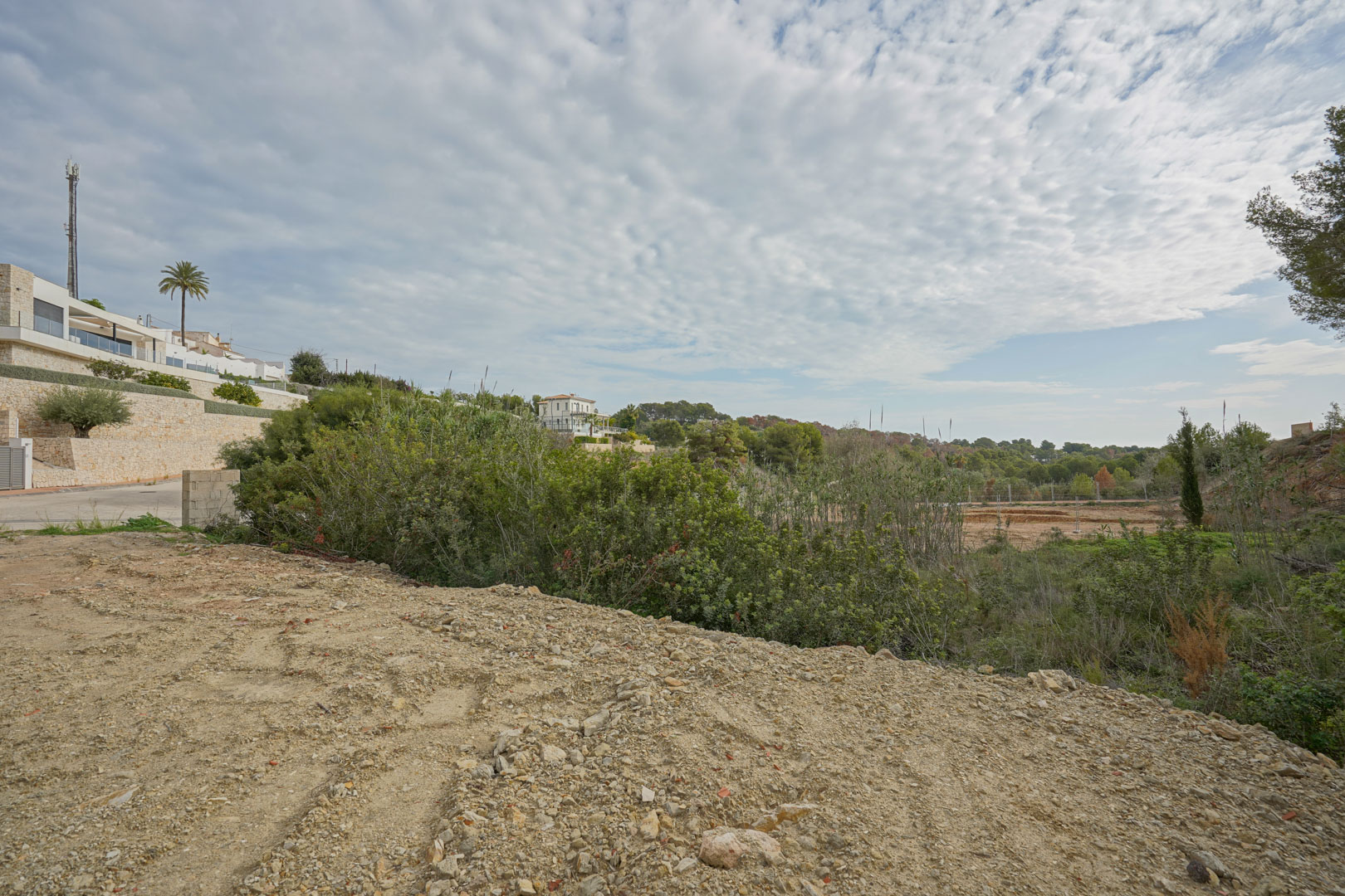 Terrain prêt à bâtir entouré de végétation méditerranéenne et de villas modernes avec murs en pierre naturelle dans un quartier résidentiel calme.