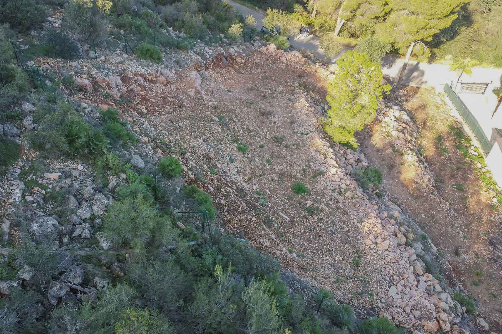 Terrain en terrasses à Montepego avec un sol rocheux dégagé, clôture périmétrale et végétation méditerranéenne, situé à proximité d'une voie d'accès.
