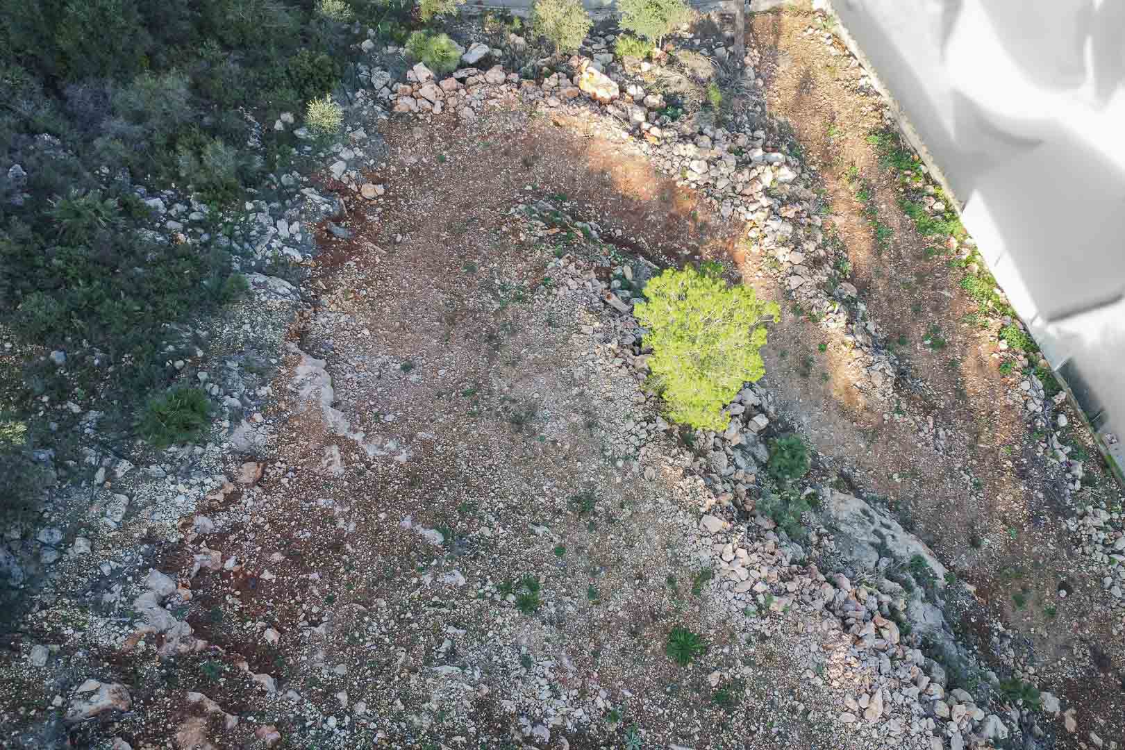 Vue aérienne du terrain à bâtir présentant un sol rocheux et une végétation méditerranéenne. La parcelle est délimitée et prête pour les travaux de construction.