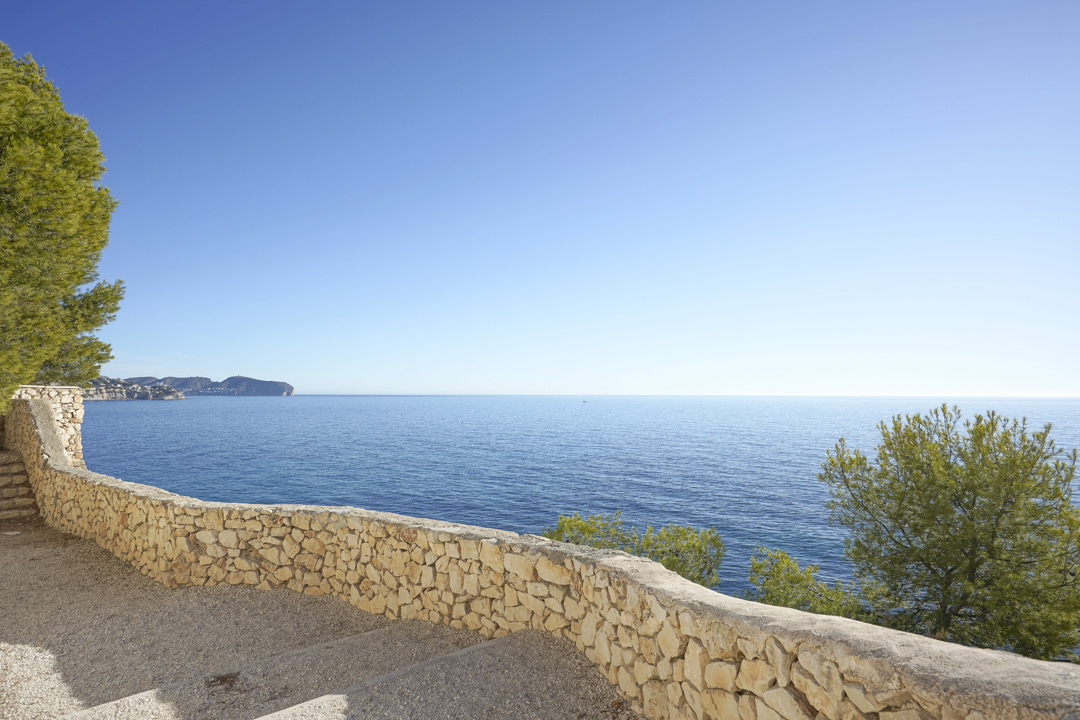 Vue panoramique sur la mer Méditerranée depuis une terrasse avec muret en pierre naturelle. Le paysage est complété par des pins et une ligne d'horizon dégagée.