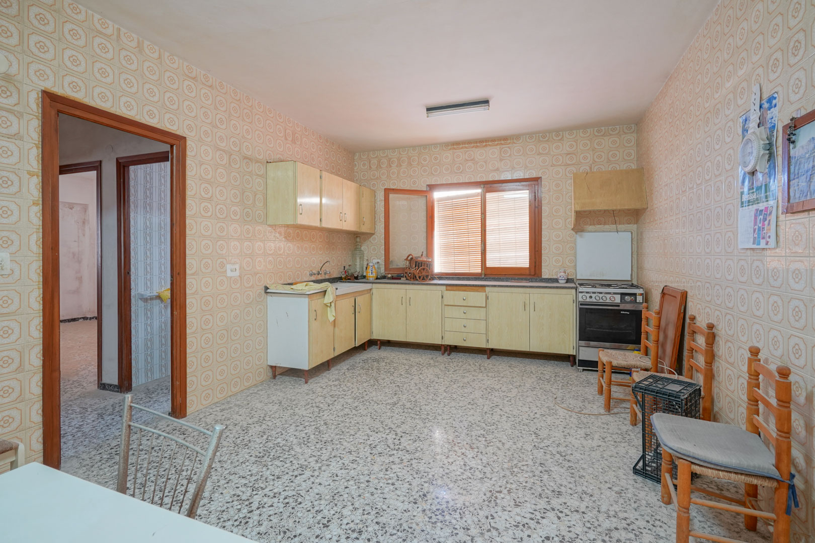 Cuisine spacieuse avec carrelage mural d'époque, sol en terrazzo et meubles en bois clair, bénéficiant d'une lumière naturelle constante par la fenêtre.