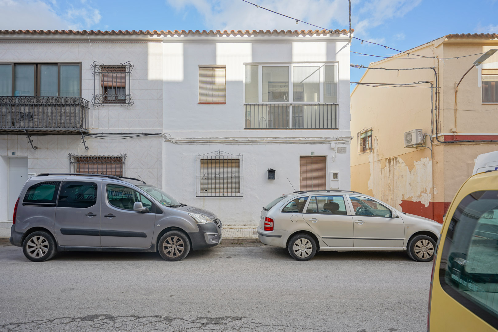 Façade extérieure de la maison de ville à Benissa avec murs blancs, grilles en fer forgé au rez-de-chaussée et une véranda vitrée à l'étage.