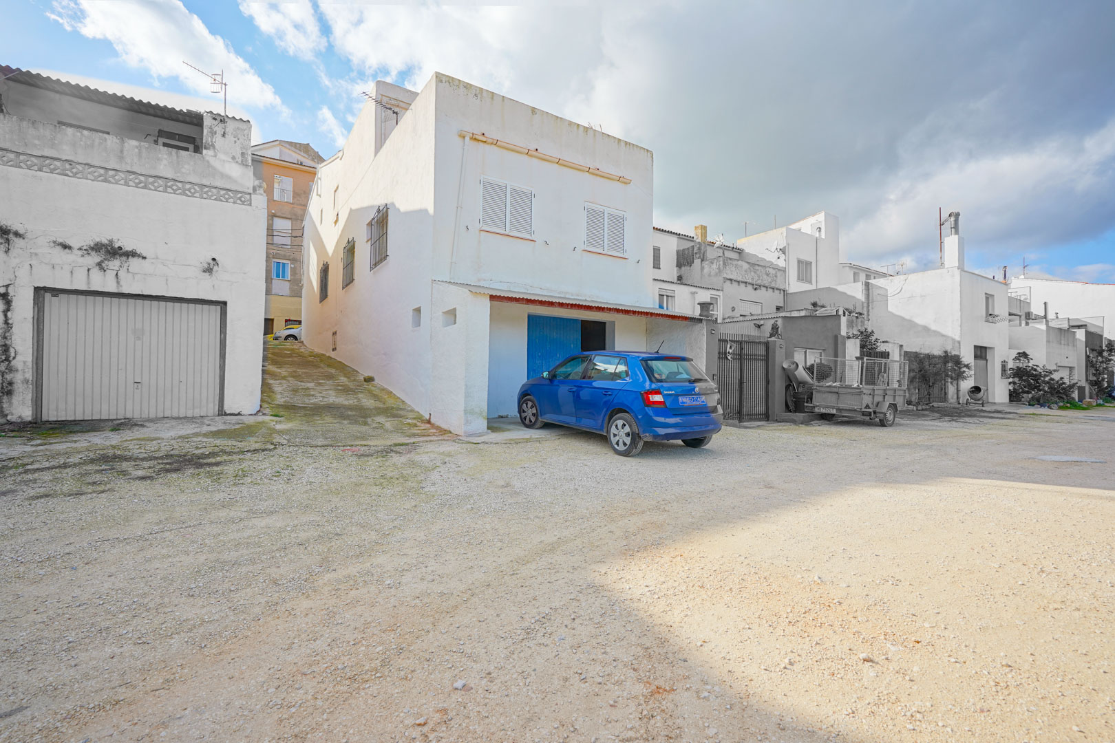Façade extérieure de la propriété à Benissa montrant l'entrée du garage en demi-sous-sol, une rampe latérale et des volets blancs.