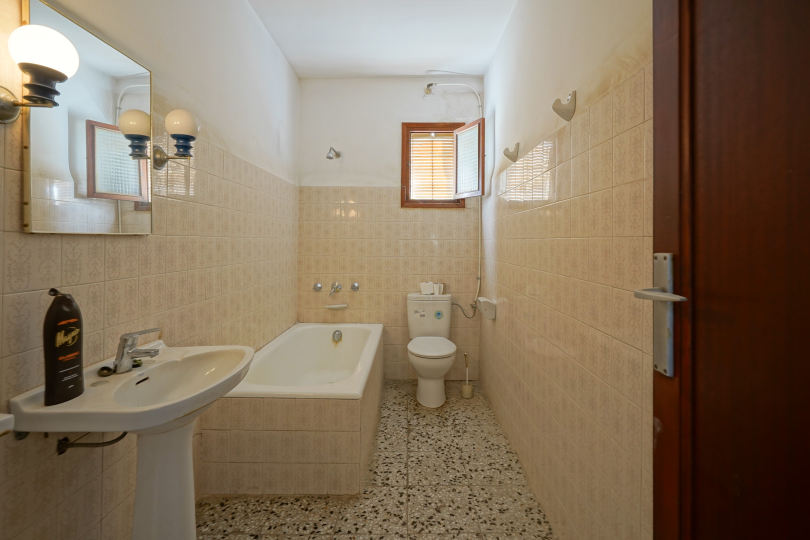 Salle de bain fonctionnelle avec baignoire encastrée, lavabo sur colonne, sol en terrazzo et carrelage mural aux motifs classiques.