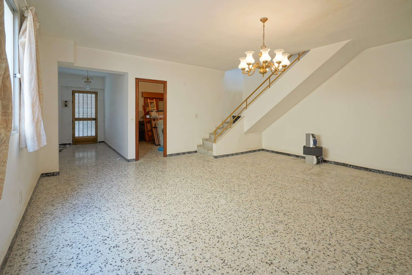 Salon principal avec sol en terrazzo d'origine, escalier intégré avec rampe métallique et accès au hall d'entrée et aux chambres.