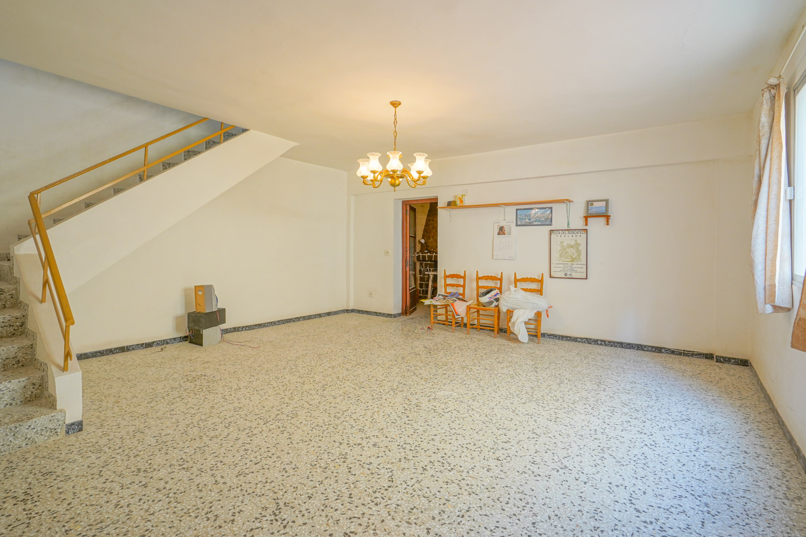 Salon principal avec sol en terrazzo d'origine, lustre classique et escalier avec rampe métallique menant à l'étage supérieur.
