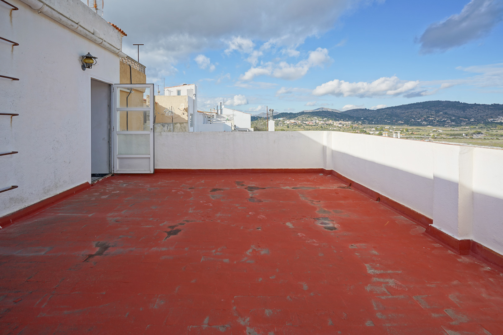 Terrasse supérieure avec revêtement de sol rouge et murs blancs, offrant une vue panoramique sur les montagnes et la campagne environnante.
