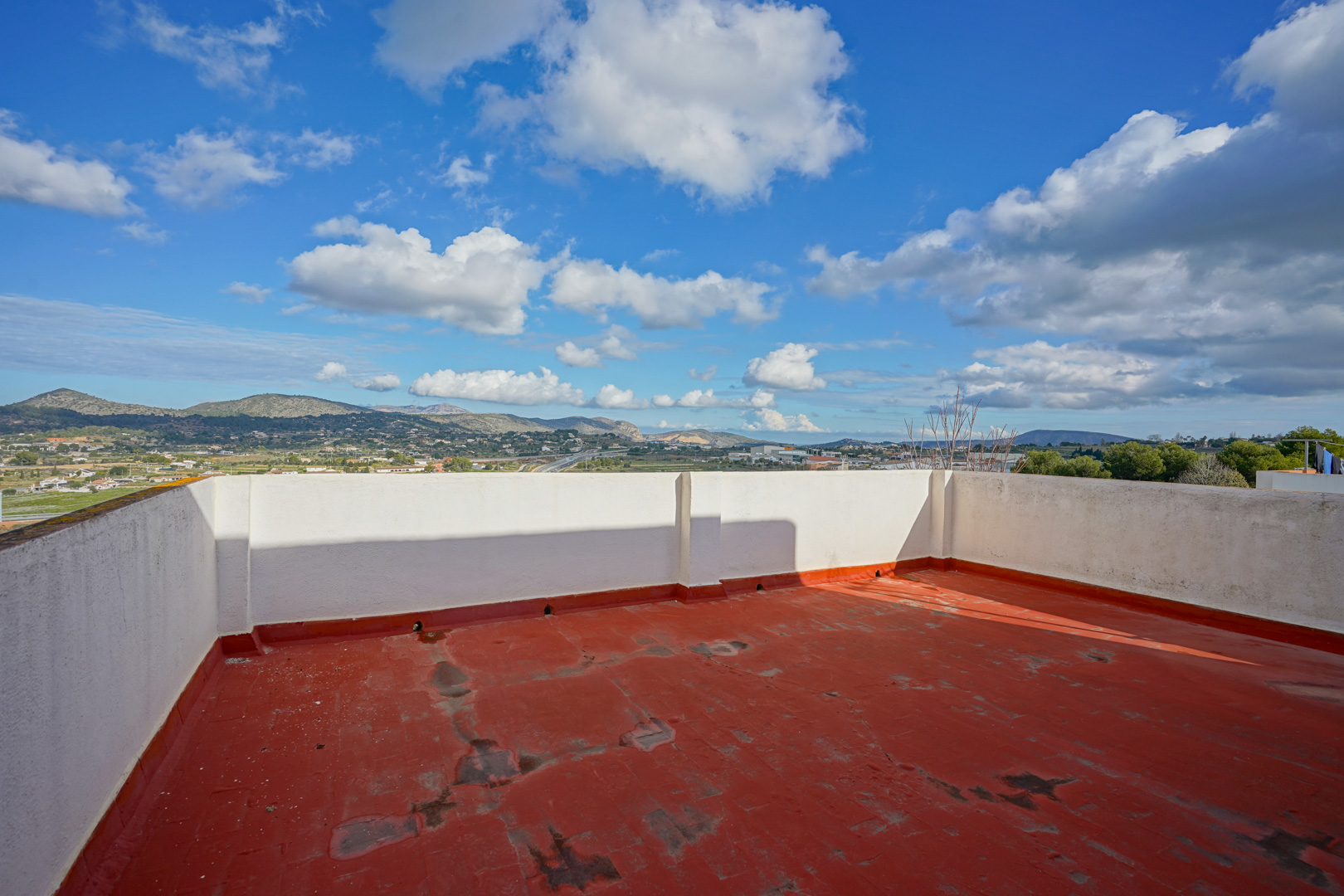 Terrasse sur le toit avec sol rouge et murets blancs, offrant une vue panoramique sur les montagnes et l'arrière-pays de Benissa.