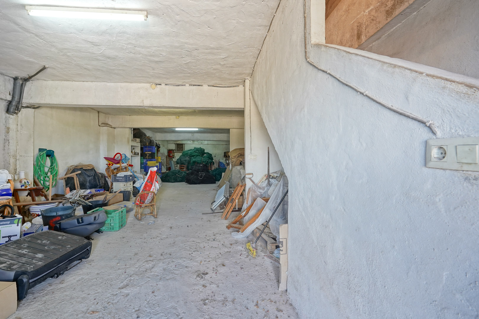 Vaste garage en semi-sous-sol avec sol en béton et murs enduits. Il dispose d'un escalier latéral permettant un accès direct aux étages supérieurs.