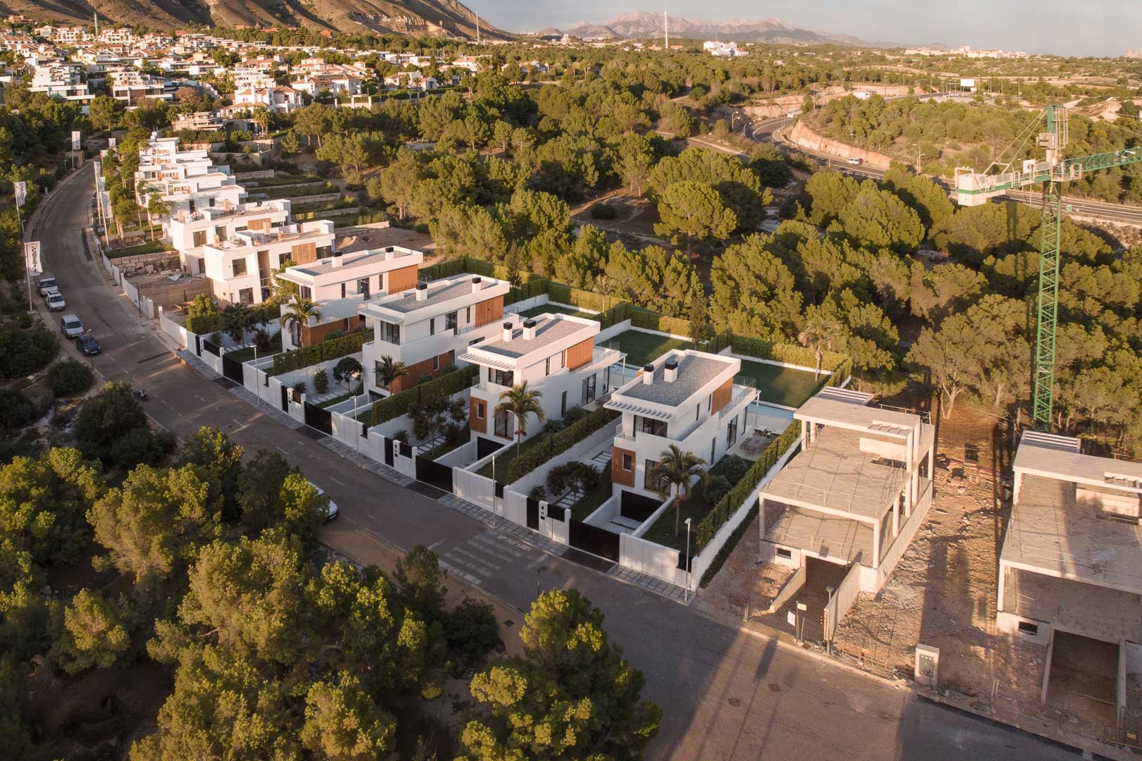 Vue aérienne du complexe résidentiel avec des villas modernes aux lignes épurées, piscines privées et jardins, entourées d'une pinède et de paysages montagneux.