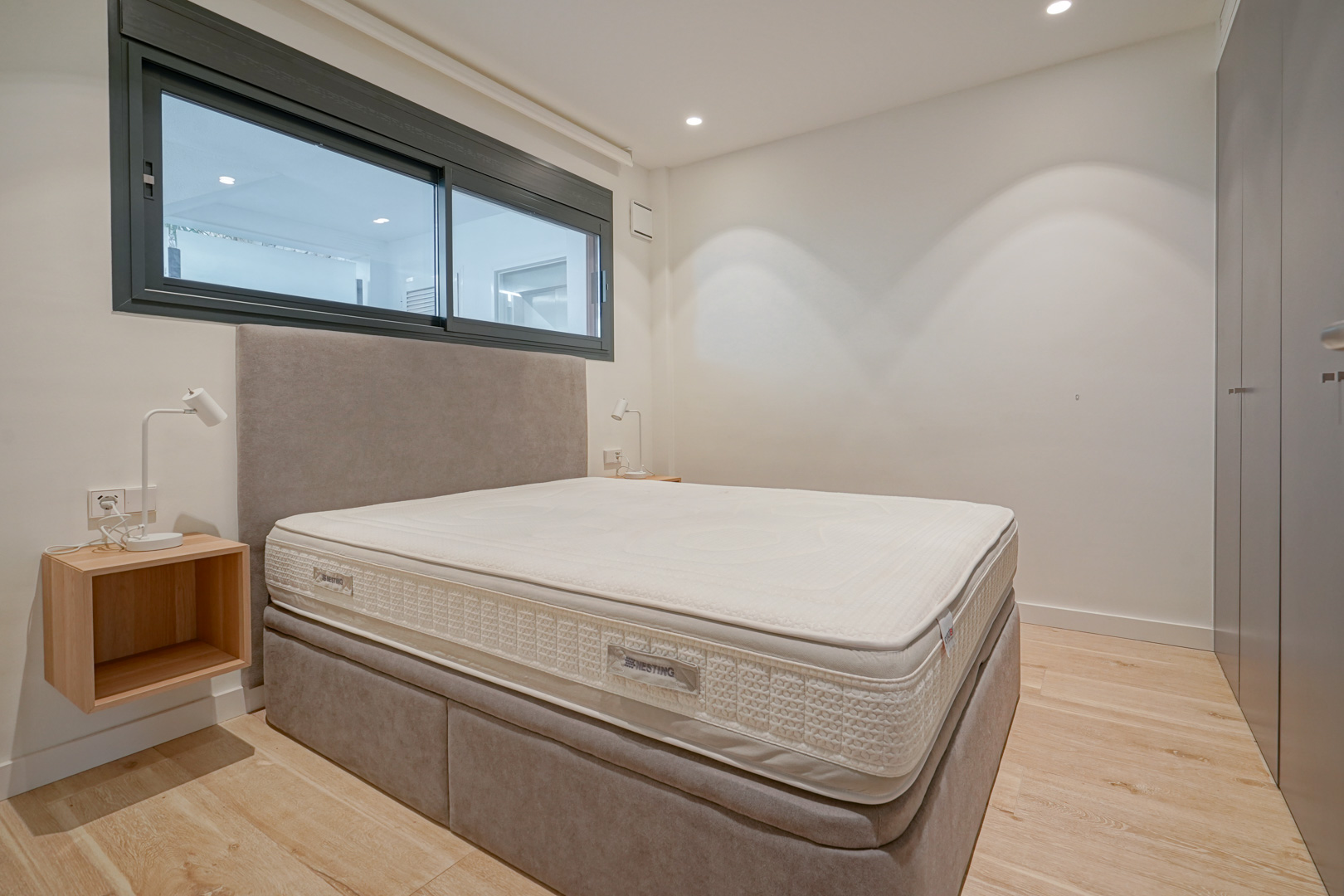 Chambre moderne avec lit double, tête de lit rembourrée, placards intégrés et parquet clair sous un éclairage encastré.
